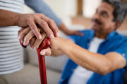 Caregiver holding care recipient's hand on cane. 